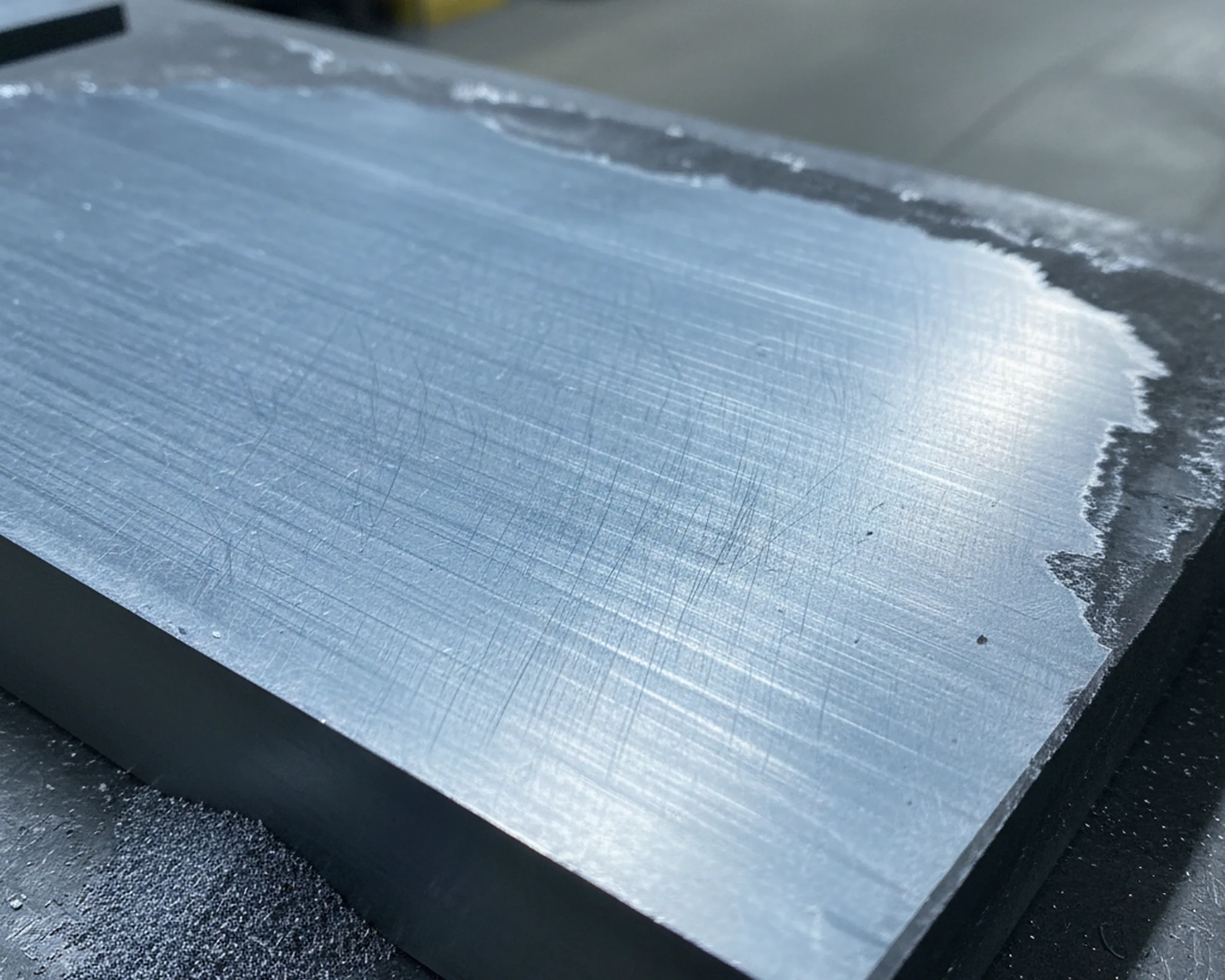 Bright ground face of a tool steel plate straight off the grinder, the forged skin already in the swarf